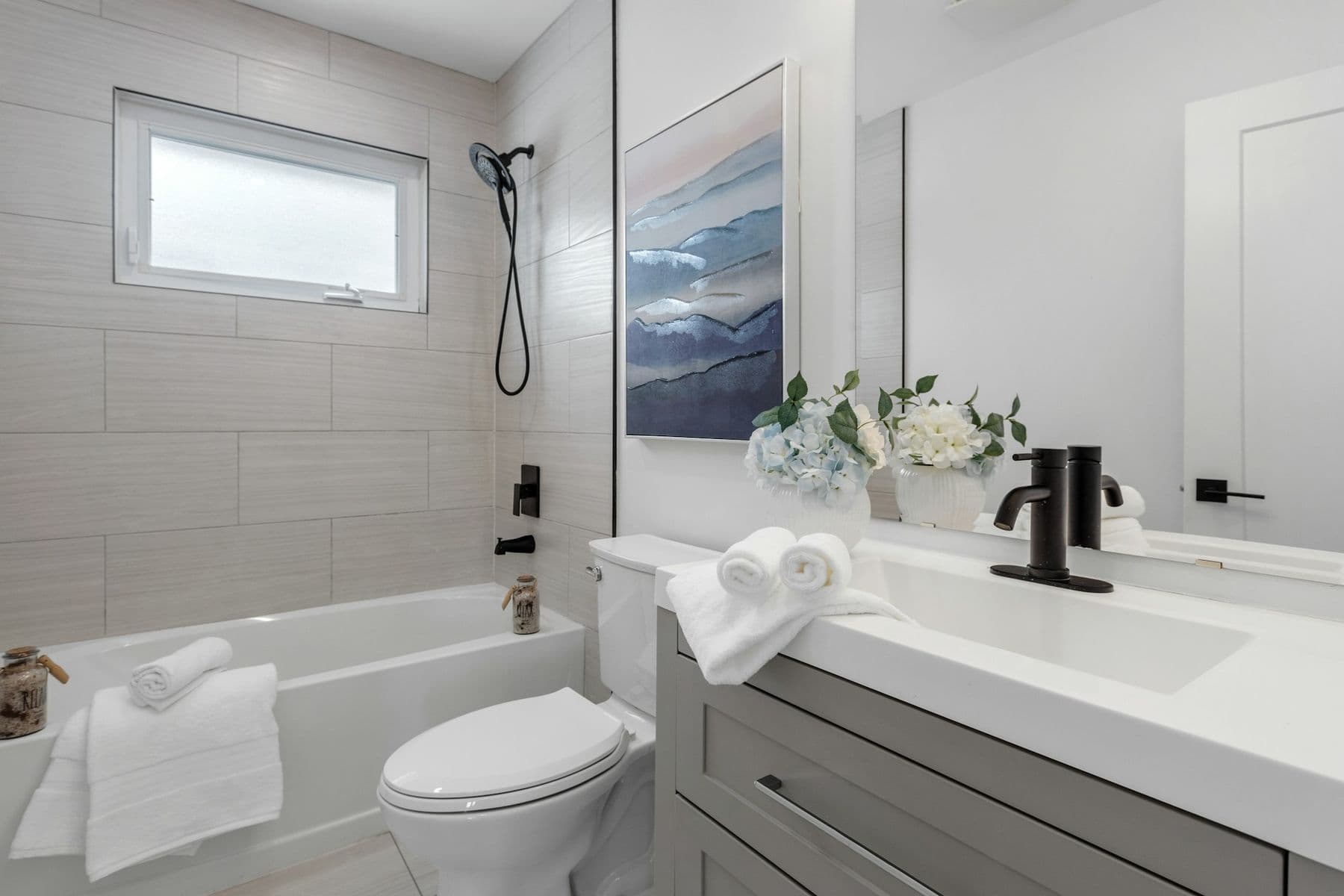 Bathtub with light gray tile surround and a white vanity