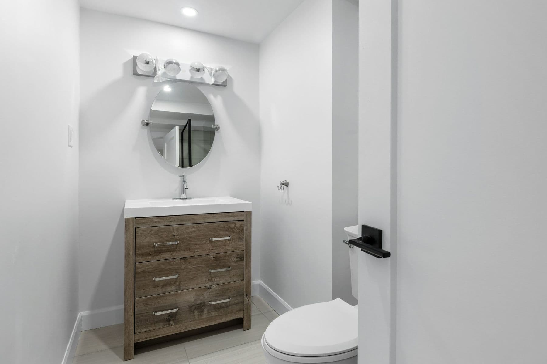 Half bath with a wood vanity, round mirror and toilet